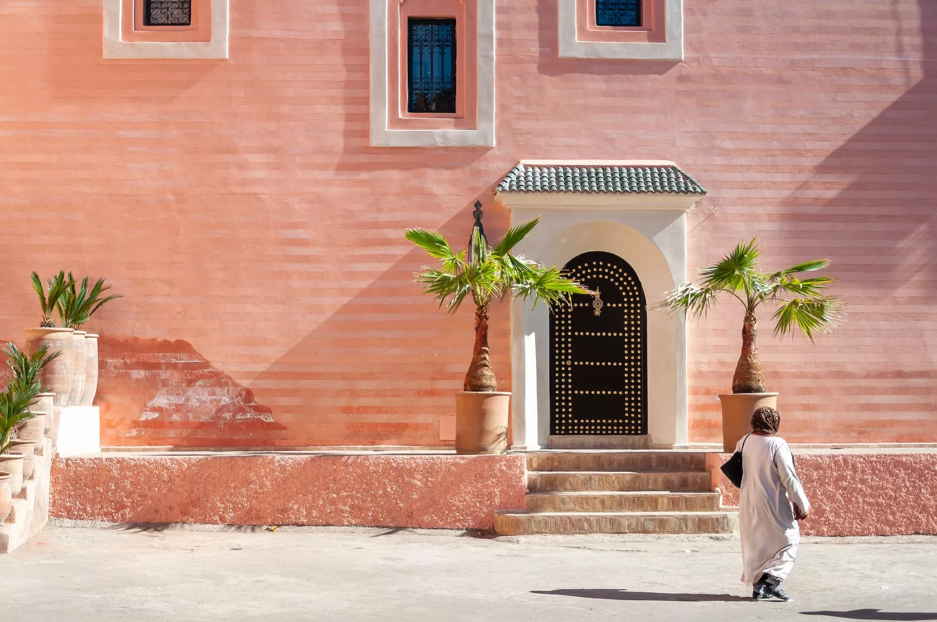 unrecognizable ethnic female in traditional hijab walking near aged building in town Jazz Club in MoroccoJazz Club in Morocco