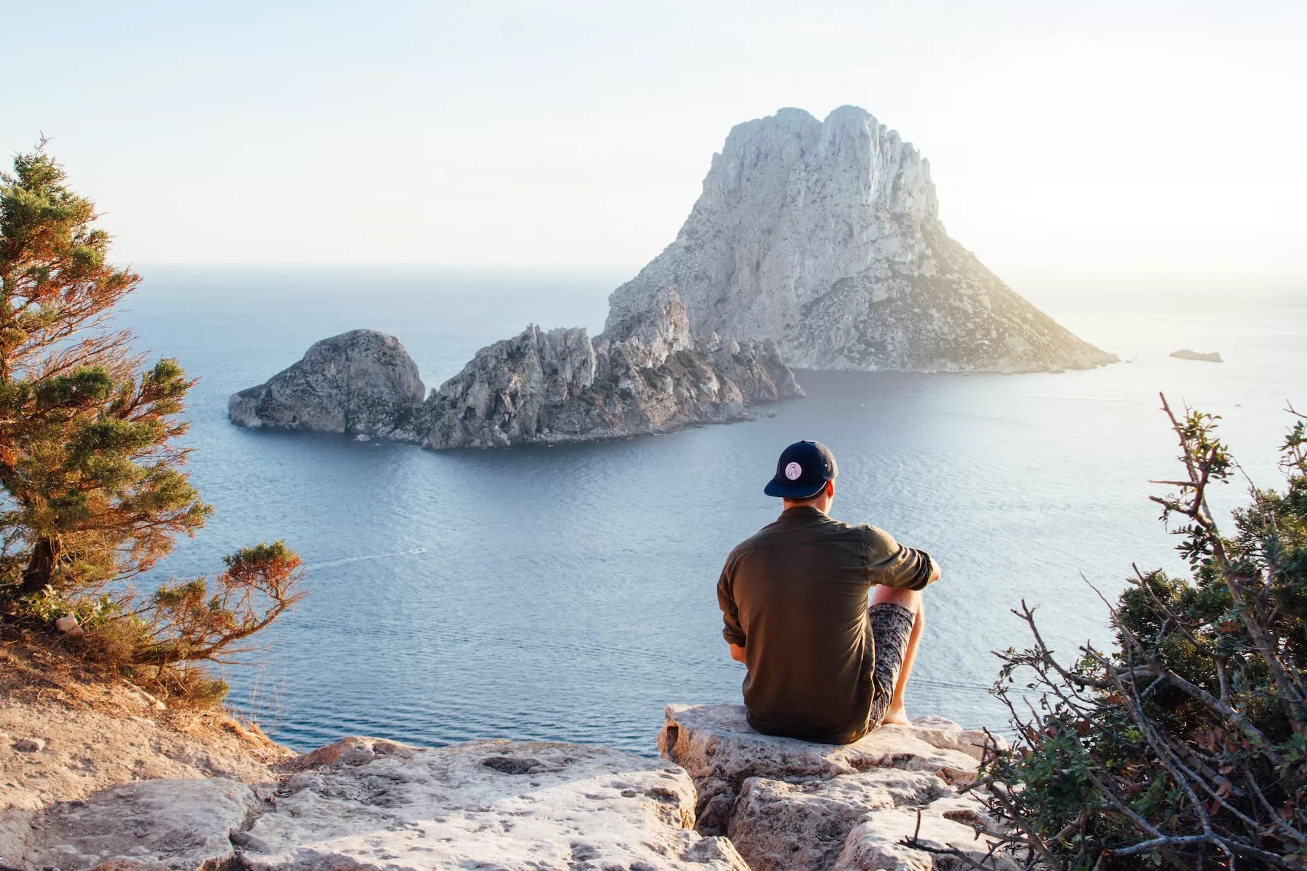 rear view of man sitting on rock by sea. Get your travel guide