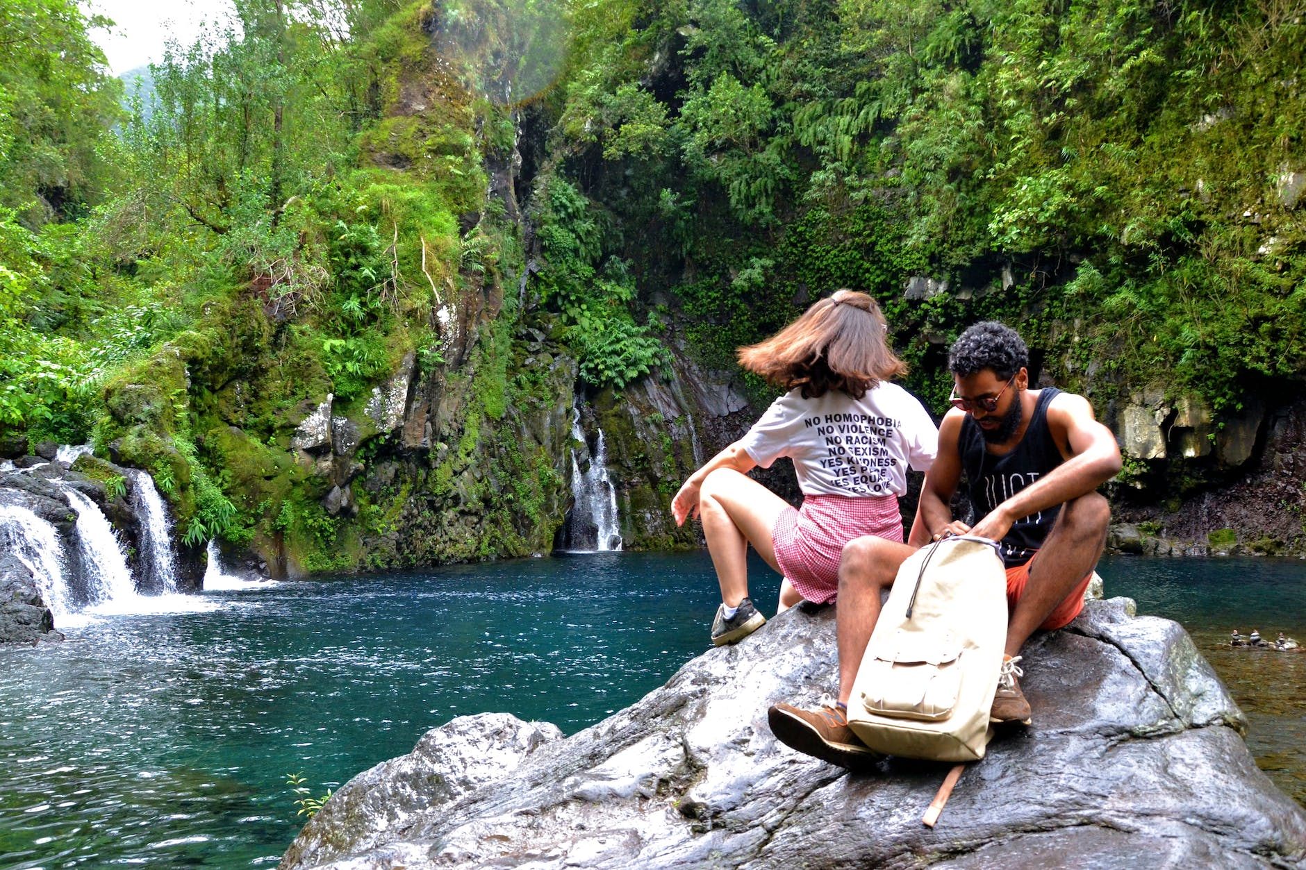 photo of couple sitting on boulder near lake