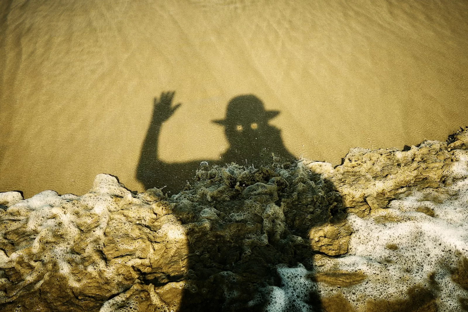 Shadow of a person in a hat waving on sand